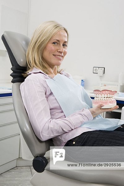 Eine Frau  die auf einem Zahnarztstuhl sitzt und Modellzähne hält.