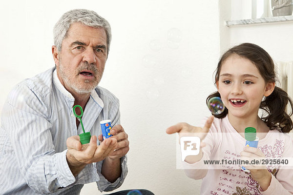 Ein Großvater und eine Enkelin spielen mit Seifenblasen.