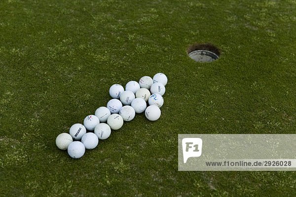 Pfeil von Golfbällen  der auf ein Loch auf einem Putting Green zeigt.