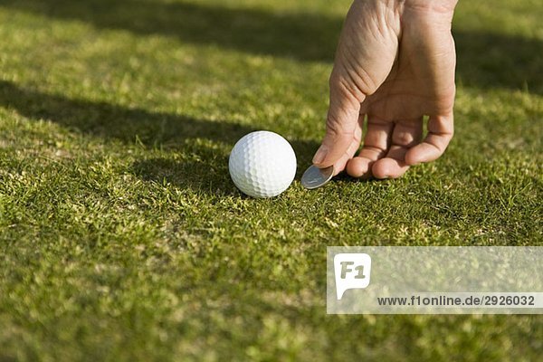 Detail eines Golfers  der die Position des Balls mit einer Münze markiert.