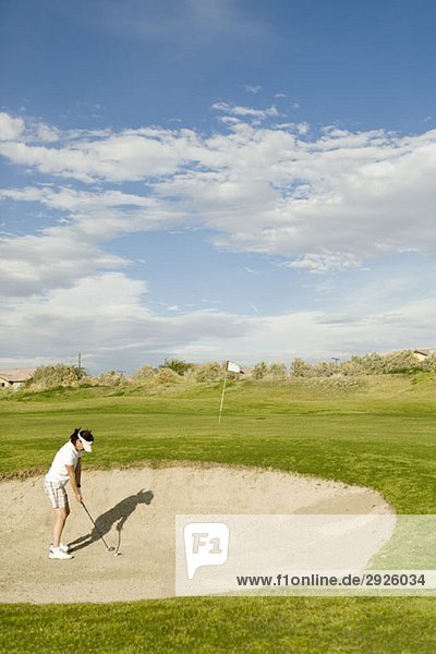 Ein Golfer  der aus einem Sandbunker spielt.