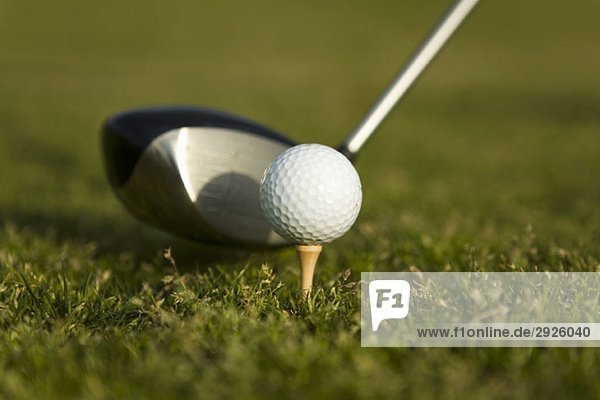 Detail eines Golfschlägers neben einem Golfball auf einem Tee