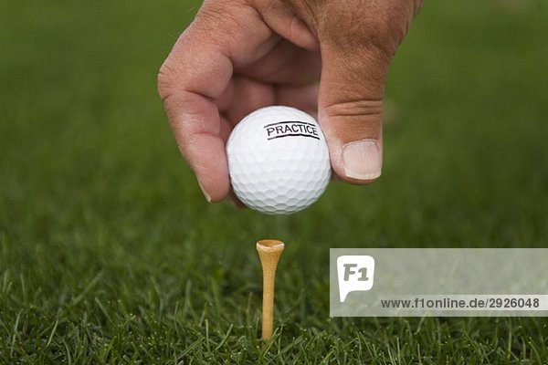 Detail eines Golfspielers  der einen Golfball auf ein Tee legt.