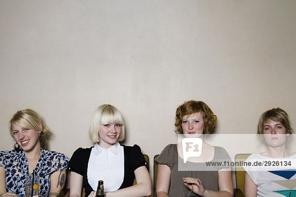 Vier junge Frauen sitzen an einer Wand in einer Bar.
