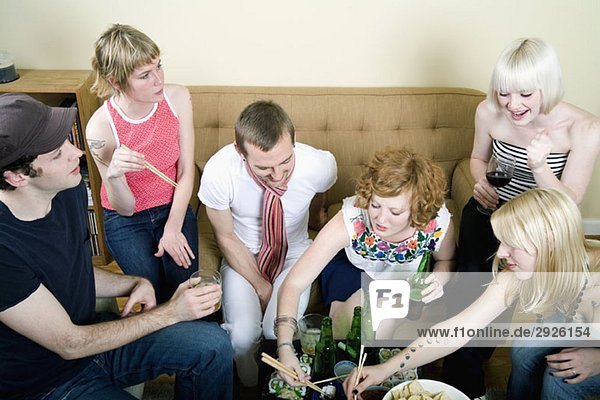 Eine Gruppe von Freunden  die in einem Wohnzimmer essen und trinken.