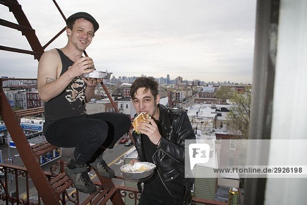 Two young men eating take out food on a fire escape