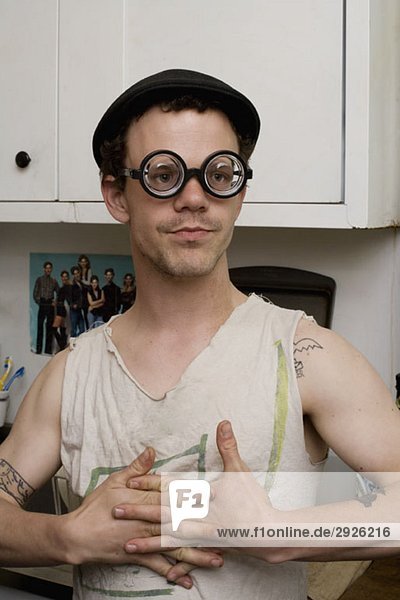 Ein junger Mann  der in einer Küche steht und eine dumme Brille trägt.