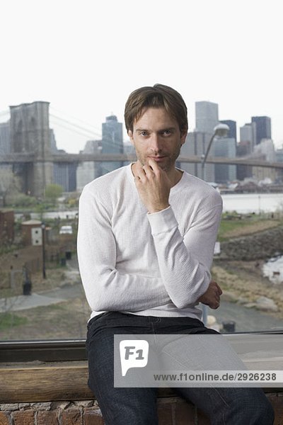 Mann sitzt auf einer Fensterbank vor der Skyline von Manhattan.