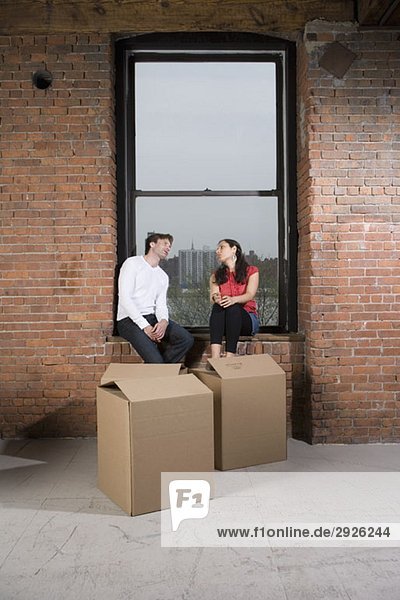A couple sitting on the window sill with cardboard boxes