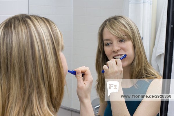 A young woman brushing her teeth in front of a bathroom mirror