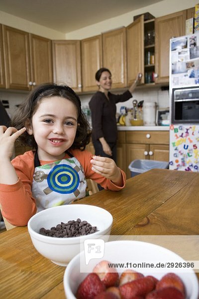 Ein junges Mädchen sitzt an einem Küchentisch und ihre Mutter steht dahinter.
