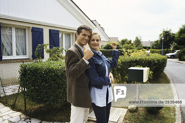Couple standing in front of house  making thumbs up gesture at camera