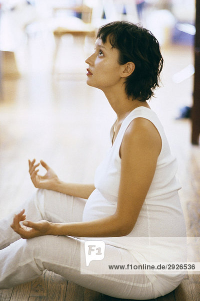 Schwangere Frau beim Meditieren auf dem Boden  Seitenansicht