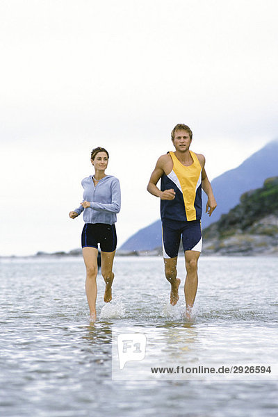 Junges Paar läuft gemeinsam durch flaches Wasser in Ufernähe