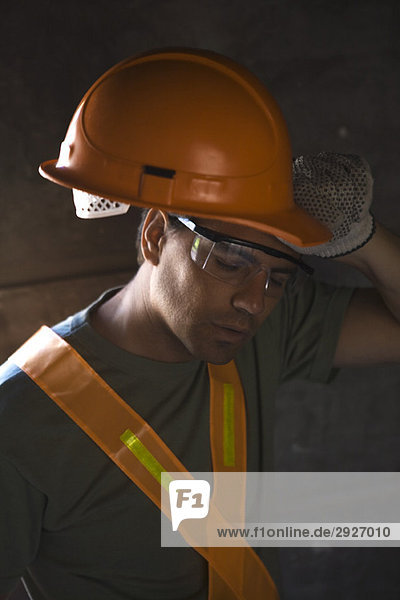 Bauarbeiter nimmt den Helm ab und wischt die Stirn mit dem Handrücken ab.