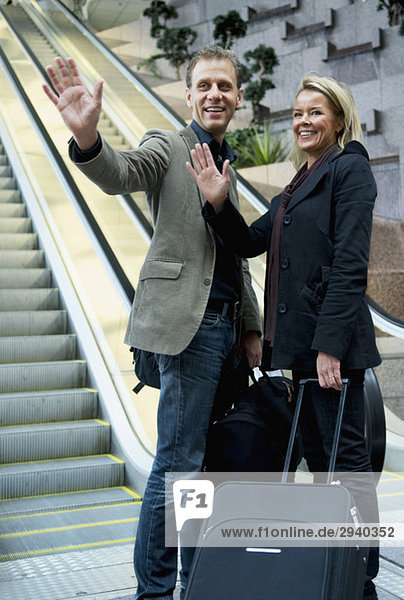 Man and woman with suitcase wave goodbye
