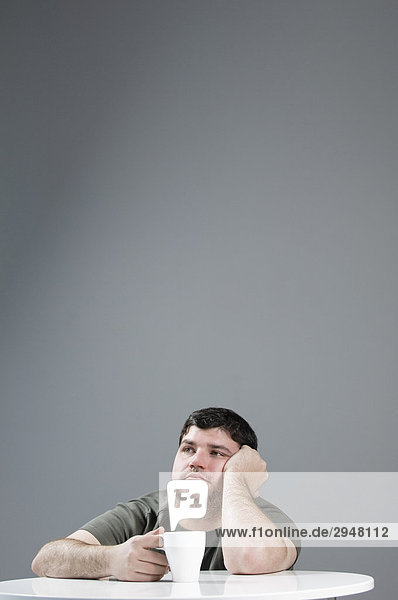 Mann mit einem Kaffee auf einer Tabelle auf einem grauen Hintergrund traurig suchen