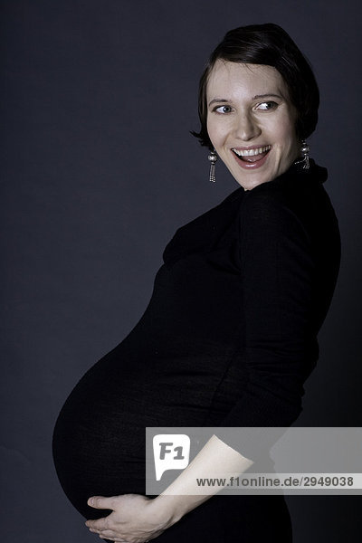 Schwangere Frau lächelnd und hält Bauch  schwarzes Kleid tragen.