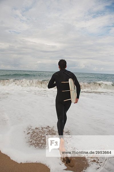 Man walking into the sea holding his surfboard