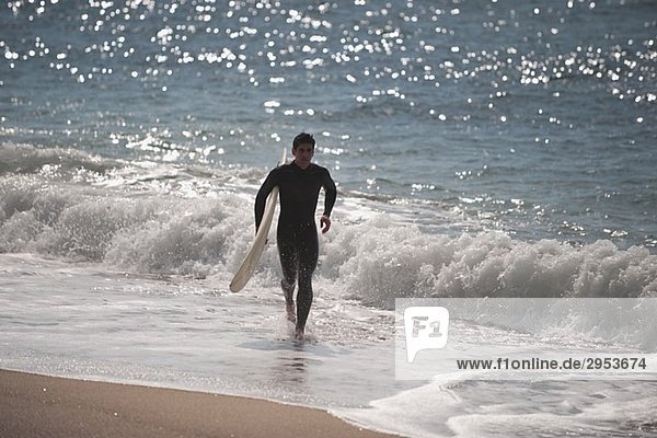 Junger Mann  die entlang der Küstenlinie mit seinem Surfbrett