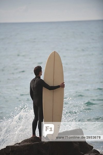 Surfer auf Rock mit Surfboard suchen auf See