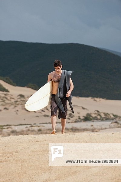 Surfer holding surfboard and walking on beach