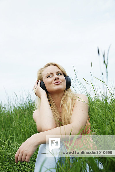 A young woman sitting in grass listening to music  low angle view