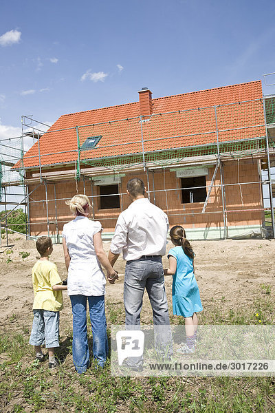 Familie mit zwei Kindern schaut auf die Baustelle eines Hauses  Rückansicht