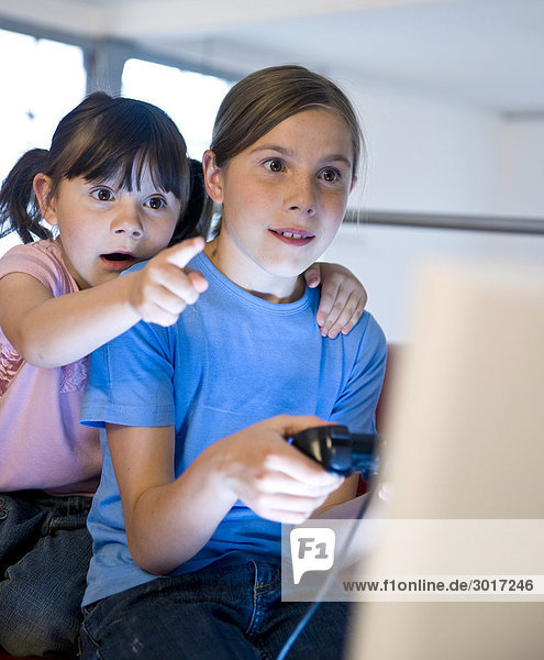 Mädchen spielt ein Computerspiel während ihre Schwester auf den Bildschirm zeigt