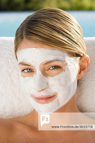 Young woman with facial mask on sitting by pool