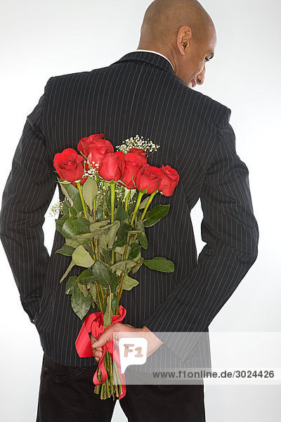 Mann mit einem Strauß Rosen hinter dem Rücken.