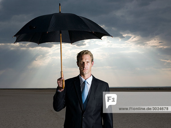 Geschäftsmann in der Wüste mit Regenschirm