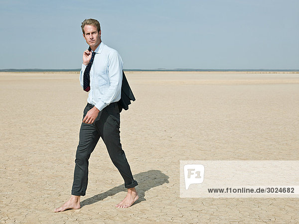 Businessman walking barefoot in the desert