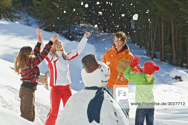 Austria  Salzburger Land  Altenmarkt  Family standing by snowman  throwing snow in the air  laughing  portrait