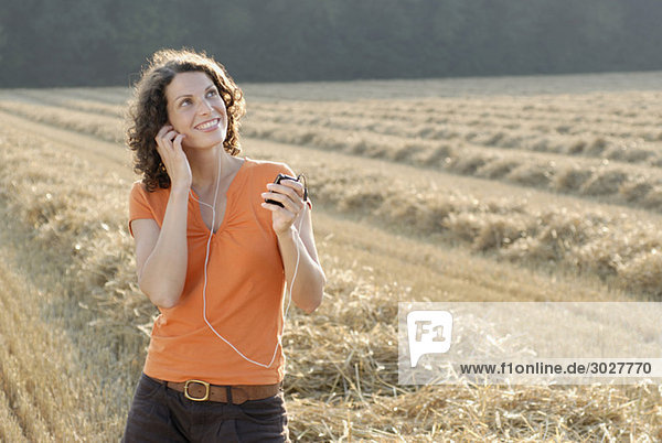Young woman in field listening to MP3 player  portrait