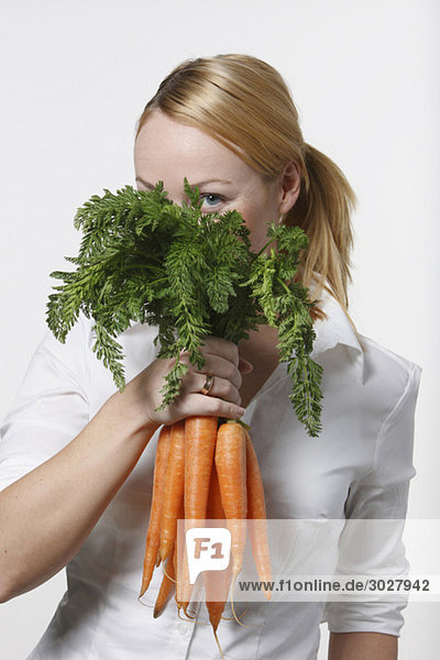 Junge Frau mit Karottenstrauß  Gesicht bedeckend  Portrait