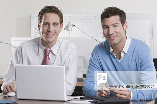 Deutschland,  München,  zwei Geschäftsleute im Büro mit Laptop,  lächelnd,  Portrait