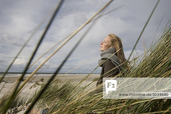 Germany  Schleswig Holstein  Amrum  Young woman on grassy sand dune  eyes closed