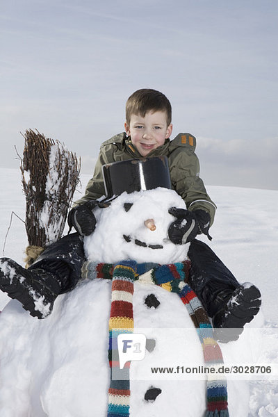 Boy (8-9) sitting on snowman  portrait