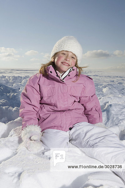 Mädchen (6-7) im Schnee sitzend  lächelnd  Porträt