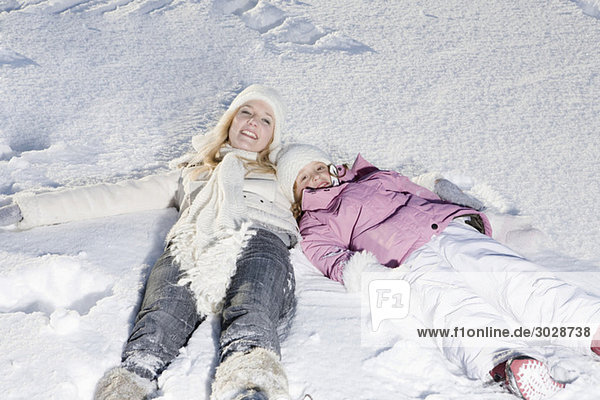 Deutschland  Bayern  München  Mutter und Tochter (6-7) im Schnee liegend  Hochansicht