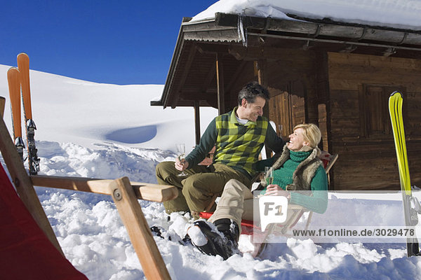 Italien  Südtirol  Seiseralm  Paar vor der Blockhütte sitzend  Sektgläser haltend  lächelnd  Portrait