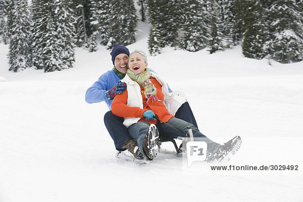 Italy  South Tyrol  Seiseralm  Senior couple sledding down hill  laughing  portrait
