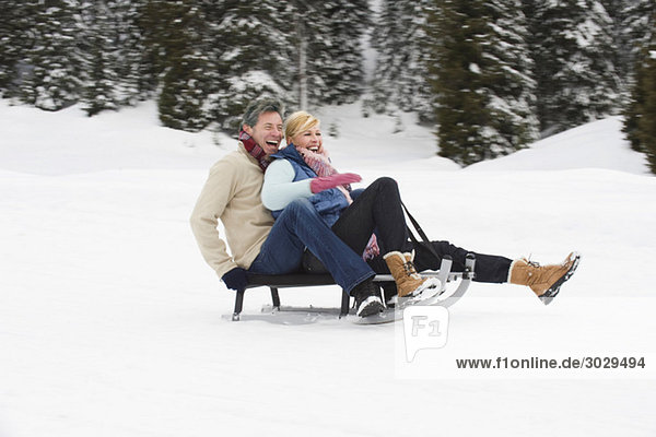 Italy  South Tyrol  Seiseralm  Couple sledding downhill  laughing  portrait