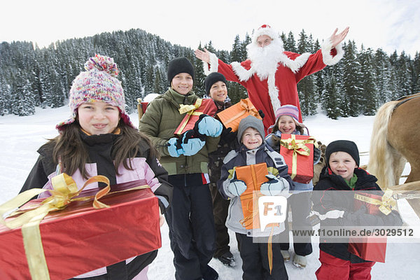 Italien  Südtirol  Seiseralm  Kinder mit Geschenkpaketen  Weihnachtsmann im Hintergrund  Portrait