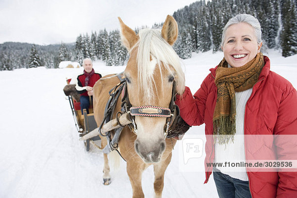 Italien  Südtirol  Seiseralm  Seniorin zu Pferd stehend  Mann im Schlitten sitzend  lächelnd  Portrait