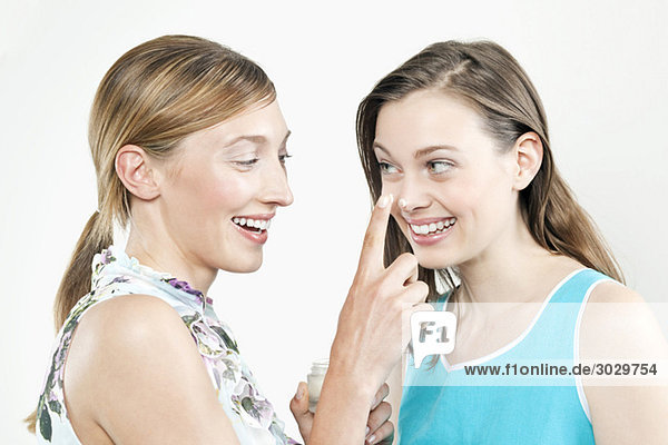 Woman putting cream on girl friends nose  smiling  portrait