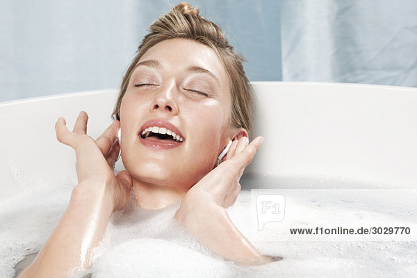 Young woman in bathtub listening to music