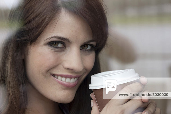 Young woman holding plastic cup of coffee  smiling  portrait
