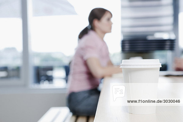 Plastikbecher im Vordergrund  Frau sitzend im Hintergrund des Cafés